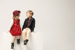 Cute stylish children on white studio background. Two beautiful teen girl and boy sittting together. Stylish young teen girl posing at studio. Sublings day. Teen and kids fashion concept. 