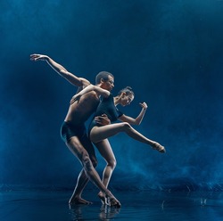 The couple of ballet dancers dancing under water drops and spray. Young caucasian and afro american models. Man and woman dancing together. Ballet and contemporary choreography concept. Art photo