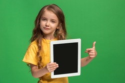 Little funny girl with tablet on green studio background. She showing something and pointing at screen.