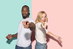 I choose you and order. The smiling mixed couple point you, want you, half length closeup portrait on studio background. The human emotions, facial expression concept. Front view. Trendy colors