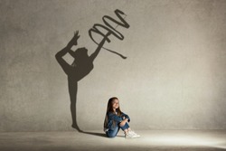 Baby girl dreaming about gymnast profession. Childhood and dream concept. Conceptual image with shadow of female gymnast on the studio wall