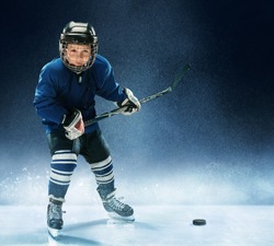 Little boy playing ice hockey at arena. A hockey player in uniform with equipment over a blue background. The athlete, child, sport, action concept