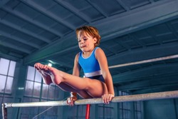 The beautiful little girl is engaged in sports gymnastics on a parallel bars at gym. The performance, sport, acrobat, acrobatic, exercise, training concept