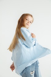 Stylish little smiling girl posing in casual clothes isolated on white studio background. Caucasian blonde female model in shirt and jeanse. Human emotions, facial expression, childhood, fashion.