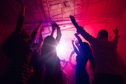 New Year's. A crowd of people in silhouette raises their hands on dancefloor on neon light background. Night life, club, music, dance, motion, youth. Purple-pink colors and moving girls and boys.