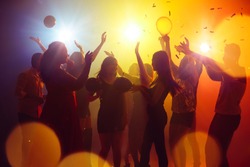 Emotions. A crowd of people in silhouette raises their hands on dancefloor on neon light background. Night life, club, music, dance, motion, youth. Yellow-blue colors and moving girls and boys.