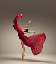 Free flight. Graceful classic ballerina dancing on grey studio background. Deep red cloth. The grace, artist, movement, action and motion concept. Looks weightless, flexible. Fashion, style.