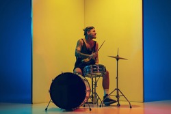 Young musician with drums performing on yellow background in neon light. Concept of music, hobby, festival, entertainment, emotions. Joyful, inspired drummer. Colorful portrait of artist.