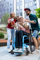 Group of friends taking a stroll on city's street in summer day. Handicapped man with his friends having fun. Inclusion and diversity concept, normal lifestyle of special groups of society.
