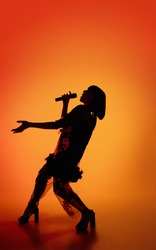 Dance. Silhouette of young female singer isolated on orange gradient studio background in neon light. Beautiful shadow in action, performing. Concept of human emotions, expression, ad, music, art.