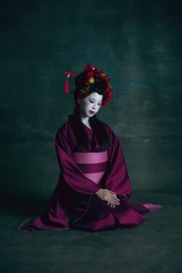 Humble. Young japanese woman as geisha isolated on dark green background. Retro style, comparison of eras concept. Beautiful female model like bright historical character, old-fashioned.