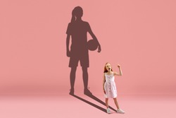 Childhood and dream about big and famous future. Conceptual image with girl and drawned shadow of basketball, soccer female player on coral pink background. Childhood, dreams, education concept.