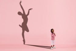 Childhood and dream about big and famous future. Conceptual image with girl and drawned shadow of female ballet dancer on coral pink background. Childhood, dreams, imagination, education concept.