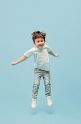 Jumping high. Happy, smiley little caucasian boy isolated on blue studio background with copyspace for ad. Looks happy, cheerful. Childhood, education, human emotions, facial expression concept.