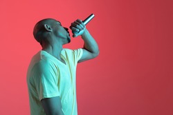 Singing, performing. African-american young man's portrait on red studio background in neon light. Beautiful male model in casual, rapping. Concept of human emotions, facial expression, youth, sales