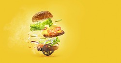 Special, express delivery. Hamburger with flying ingredients on yellow studio background. Bun, salad, meat, cheese and tomatos, onion in flight. Fast food, advertising concept. Copy space for ad.