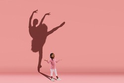 Silhouette of beautiful ballerina. Childhood and dream about big and famous future. Conceptual image with girl and shadow of female ballet dancer on coral pink wall. Sport, dreams, education concept.