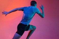 Back view. Portrat of Caucasian male athlete, runner training isolated on pink studio background with blue neon filter, light. Concept of action, motion, speed, healthy lifestyle. Copyspace for ad.