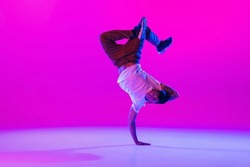 Street dance style. Young stylish man, hip-hop dancer dancing in modern clothes isolated over bright magenta background at dance hall in neon light. Youth culture, moves and fashion, action.