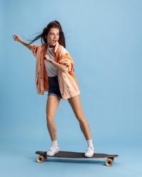 Stylish hairdo. Adorable young girl in retro 90s fashion style, outfits on skateboard isolated over pink studio background. Concept of eras comparison, beauty, fashion and youth. Looks excited
