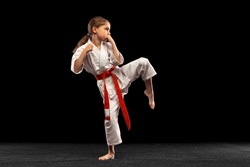 Practice. Karate, taekwondo girl with yellow belt isolated on dark background in neon light. Little female model, sport kid training in motion and action. Sport, movement, childhood concept.