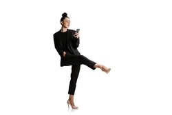 Female ballet dancer in black suit using phone. Studio shot of young woman in business style attire in action, motion isolated on white background. Art, sport, beauty, fashion concept. Copy space for