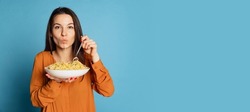 Looks very tasty. Beautiful young girl eating delicious Italian pasta isolated on blue studio background. Holidays, traditions, food, popularity, cafe, love. Healthy carbohydrates. Copy space for ad