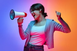 Attention, news. Excited young beautiful girl in warm cardigan shouting at megaphone isolated on gradient blue orange neon background. Concept of emotions, facial expression, youth, aspiration, sales