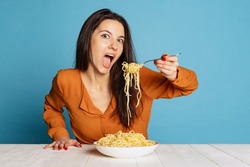 Looks very tasty. Beautiful young girl eating delicious Italian pasta isolated on blue studio background. Holidays, traditions, food, popularity, cafe, love. Healthy carbohydrates. Copy space for ad