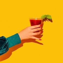 Cheers. Woman's hand with bloody mary glass isolated on bright yellow neon background Concept of taste, alcoholic drinks. Complementary colors, blue, yellow and green. Pop art. Copy space for ad, text