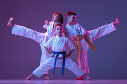 Three sportive kids, little boys, taekwondo or karate athletes in doboks posing isolated on very peri color background in neon. Concept of sport, education, skills, martial arts, healthy lifestyle and