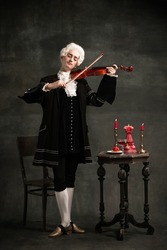 Young man in image of Amadeus Mozart, medieval person isolated on dark vintage background. Retro style, comparison of eras concept. Elegant male model as historical character, great music compose