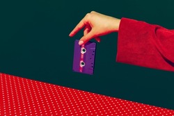 Female hand holding tape recorder cassette isolated on green and red background. Vintage, retro fashion style. Retro objects, gadgets. Vintage, retro 80s, 70s style. Concept of memory, nostalgia