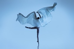 Freedom. Portrait of flexible woman, graceful ballerina dancing with fabric, cloth isolated on blue studio background. Grace, art, beauty, contemp dance, ad concept. Monochrome. Copy space for ad