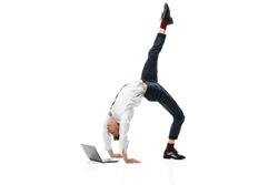 Creative portrait of young flexible man doing backbend and typing on laptop isolated over white studio background. Finance, ballet, art, business, beauty, fashion concept.