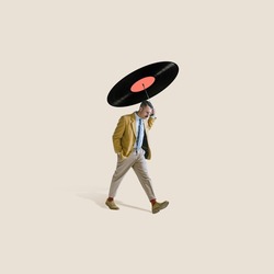 Contemporary art collage. Stylish thoughtul man walking under retro vinyl record isolated over light gray background. Musician. Concept of creativity, party, fashion. Copy space for ad
