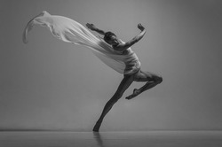 Hope. Black and white portrait of graceful muscled male ballet dancer dancing with fabric, cloth isolated on grey studio background. Grace, art, beauty, contemp dance concept. Lightness