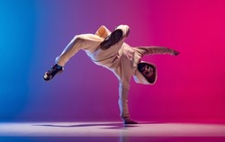 Hand stand. Studio shot of young flexible sportive man dancing breakdance in white outfit on gradient pink blue background. Concept of action, art, beauty, sport, youth. Dancer shows breakdance