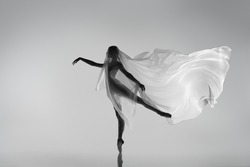 Lightness movements. Black and white portrait of graceful ballerina dancing with fabric, cloth isolated on grey studio background. Grace, art, beauty, contemp dance concept. Weightless, flexible