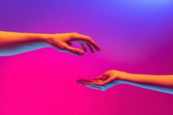 Love, care. Two authentic hands trying to touch each other isolated on gradient background in neon light. Concept of relationship, community, care, support, symbolism, culture
