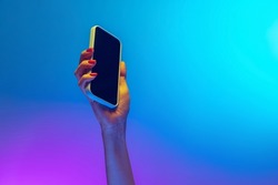 News. Closeup female hands holding gadget, smartphone isolated on gradient blue and purple background in neon. Concept of mobile lifestyle, digital technology, social gathering.