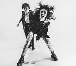 Monochrome portrait of crazy musicians, young couple wearing black leather outfits gesturing, moving on white studio background. Concept of style, art, fashion and youth, ad