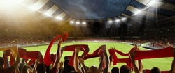 Win, victory of favourite team. Back view of football, soccer fans cheering their team with red scarfs at crowded stadium at evening time. Concept of sport, cup, world, event, competition