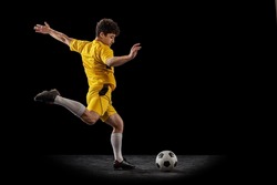 Dynamic portrait of professional football, soccer player training with ball isolated on dark background. Concept of sport, match, ad, active lifestyle. Sportsmen bright yellow football kit.