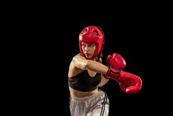 Quick attack. Female boxer in boxing gloves and helmet training isolated on dark background. Sport, competition, hobby, results, success concept. Sportive girl practicing in boxing. Copy space for ad