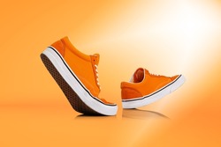 Sunny day. Modern unisex footwear, sneakers isolated on orange background. Fashionable stylish sports casual shoes. Creative minimalistic layout with footwear. Mock up for design, ad for shoe store