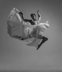 Hope. Black and white portrait of graceful muscled male ballet dancer dancing with fabric, cloth isolated on grey studio background. Grace, art, beauty, contemp dance concept. Lightness