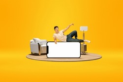 Positive young boy lying on huge 3D model of mobile phone with empty screen for text, ad over bright yellow background with home interior. Online shopping, delivery. Mockup for ad, design, logo.