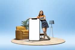 Young positive happy smiling girl standing near huge 3D model of phone screen on blue background with home interior. Online shopping. Mockup for ad, design, logo. Empty screen with copy space for text