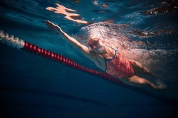 Dynamic shot of professional female swimmer training in swimming pool indoor. Developing speed. Underwater view. Concept of sport, endurance, competition, energy, healthy lifestyle